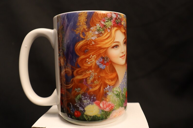 May include: White ceramic mug featuring a colourful image of a woman with long red hair wearing a flower crown. The image is surrounded by flowers and greenery.