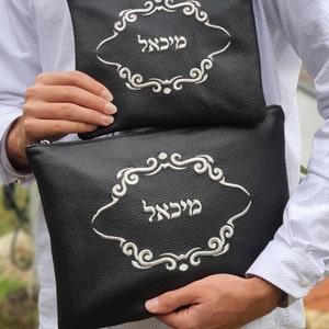 May include: Two black leather pouches with silver embroidery. The larger pouch has the Hebrew word "Melech" embroidered on it. The smaller pouch has the Hebrew word "Melech" embroidered on it.