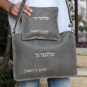 May include: A gray leather bag with a smaller gray leather pouch attached. Both items have white embroidery that reads "שלום לך" and "יבורך ה' ישמריך".