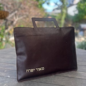 May include: A brown leather bag with a handle and the Hebrew text "מגוד יחד" embroidered on the front.