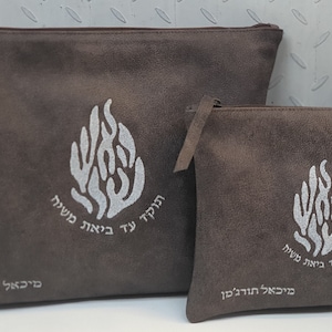 May include: Two brown suede zippered pouches with a silver flame design and Hebrew text. The larger pouch has the text "Hodah Ya Hashem" and the smaller pouch has the text "Hodah Ya Hashem Mi Ba'al Chesed."