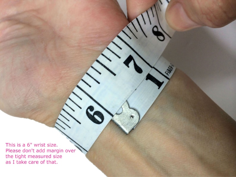 Op de afbeelding: Een witte meetlint gewikkeld om een pols, met een meting van 6 inch. De tekst "This is a 6" wrist size. Please don't add margin over the tight measured size as I take care of that." staat onder de afbeelding.