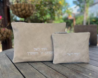 Puede incluir: Dos bolsas de gamuza beige con cremalleras plateadas. La bolsa más grande tiene texto hebreo bordado. La bolsa más pequeña también tiene texto hebreo bordado. Ambas bolsas están sobre una mesa de madera.