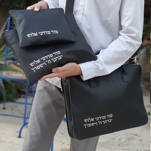 May include: Three black leather bags with Hebrew text embroidered in white. The largest bag has a strap and the smaller bags are nested inside.