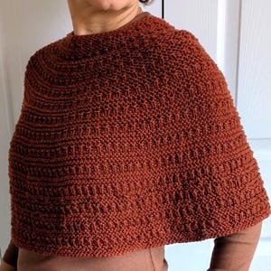 Pode incluir: Um poncho de malha na cor ferrugem com um padr&atilde;o texturizado de carreiras horizontais de pontos. A pe&ccedil;a possui um decote redondo, cobre a parte superior do tronco e apresenta uma constru&ccedil;&atilde;o de malha consistente.