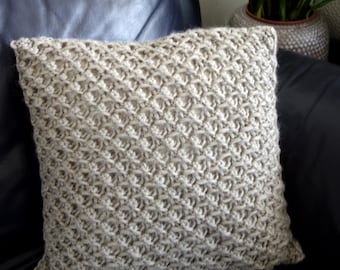 May include: A beige knitted cushion with a diamond pattern sits on a dark blue leather sofa.