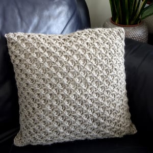 May include: A beige knitted throw pillow with a diamond pattern sits on a dark blue leather couch.
