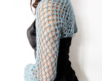 May include: A light blue crochet shrug with a delicate openwork pattern. The shrug has long sleeves and is worn over a black dress.