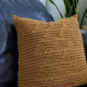 Puede incluir: Una almohada de punto marrón con un patrón geométrico. La almohada está sentada en un sofá azul oscuro.