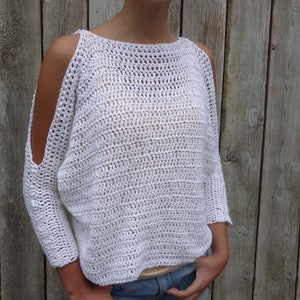 May include: White crochet top with a loose fit and cold shoulder design. The top has a wide neckline and is made with a delicate open stitch pattern.