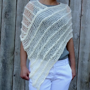 May include: A white crocheted poncho with a textured design. The poncho is made of a lightweight yarn and has a loose, flowing fit.