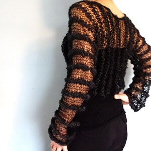 May include: A black, open-knit sweater with a loose fit and long sleeves. The sweater has a striped pattern and is made of a soft, lightweight yarn.