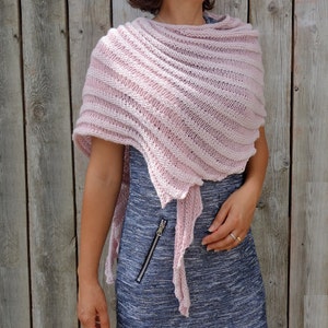 May include: A pink knitted shawl with a delicate, openwork design. The shawl is draped over a person's shoulders and is tied at the neck.