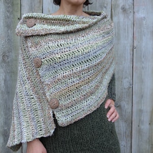 Può includere: Uno scialle all'uncinetto con collo a lupetto e bottoni in legno. Lo scialle è realizzato in una varietà di tonalità di verde, marrone e bianco.