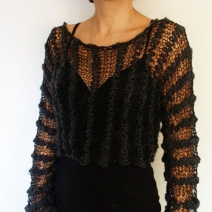 May include: A black, open-knit sweater with long sleeves. The sweater has a loose fit and a cropped length.