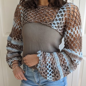 May include: A brown and blue crochet top with long sleeves and a cropped design. The top features a delicate openwork pattern and a contrasting color stripe detail.