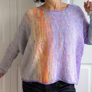 Pode incluir: Um suéter de malha roxo, laranja e branco com um caimento solto e mangas compridas.