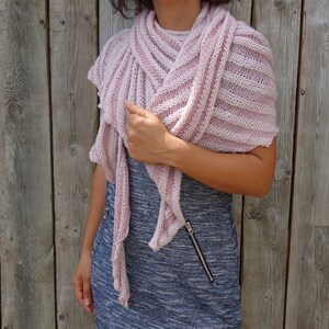 May include: A pink knitted shawl with a striped pattern. The shawl is draped over a person's shoulders and is worn with a blue and white dress.