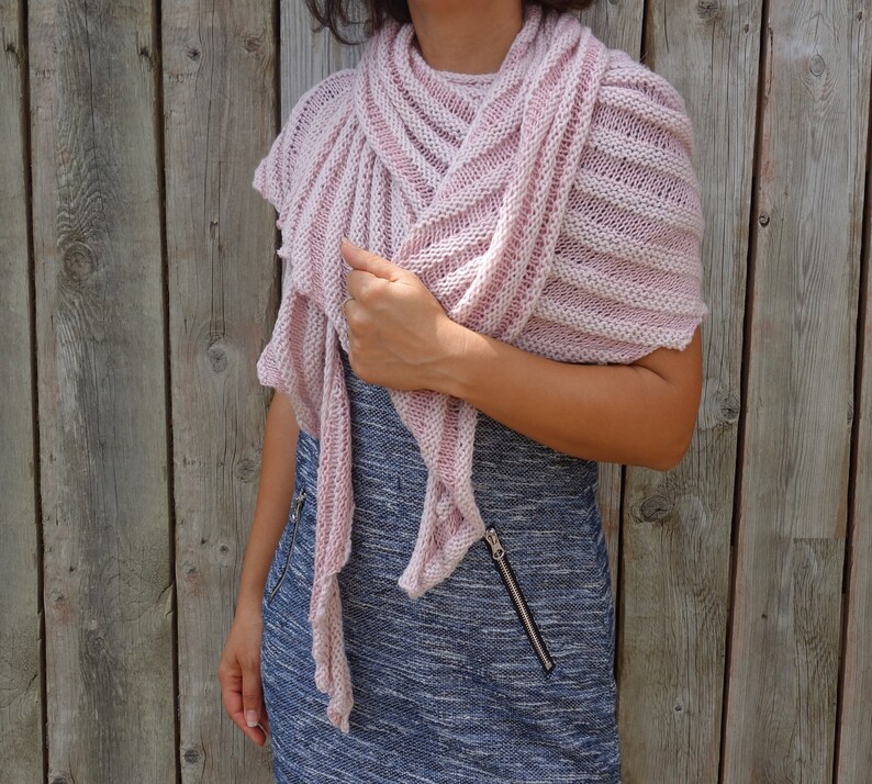 May include: A pink knitted shawl with a striped pattern. The shawl is draped over a person's shoulders and is worn with a blue and white dress.