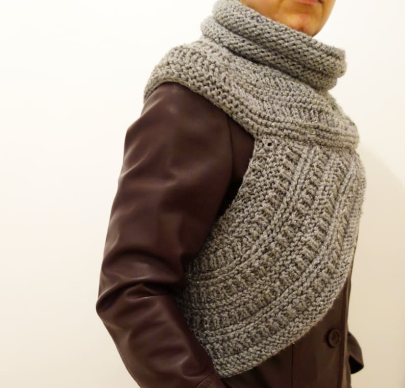 Puede incluir: Una bufanda de cuello de tortuga de punto gris con un patr&oacute;n texturizado. La bufanda se lleva sobre una chaqueta de cuero marr&oacute;n.