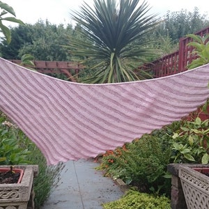 May include: A pink knitted shawl with a striped pattern, draped over a bush in a garden setting.