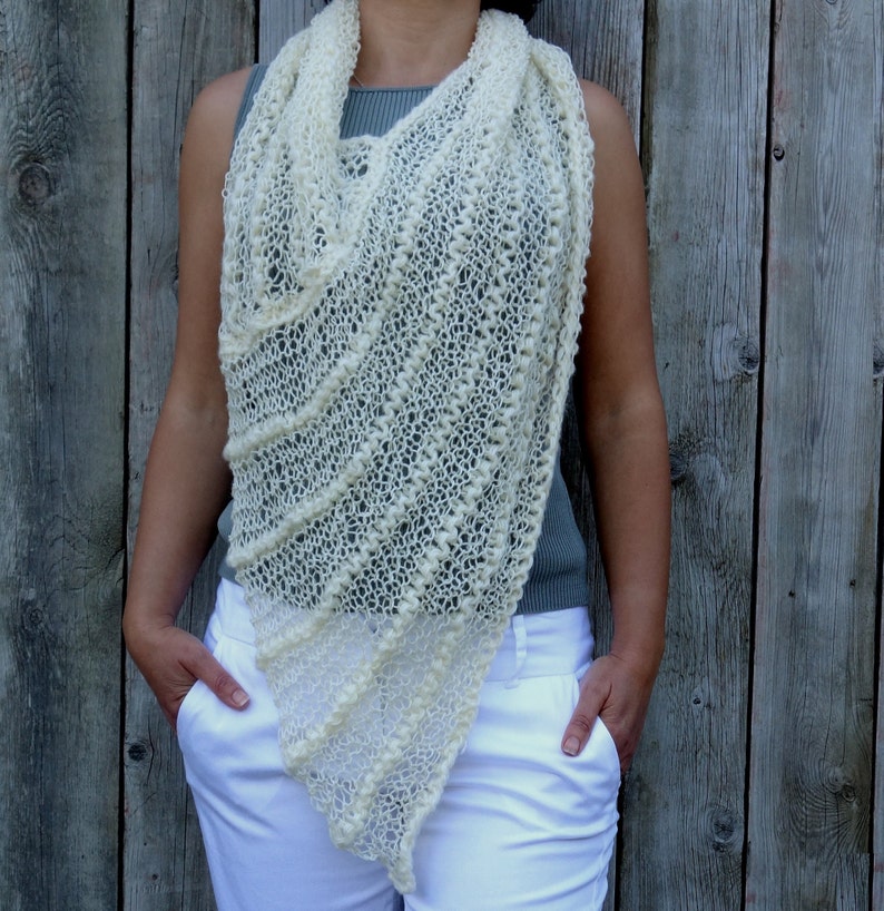 May include: A white crocheted shawl with a delicate openwork pattern. The shawl is draped around a person's shoulders and neck.