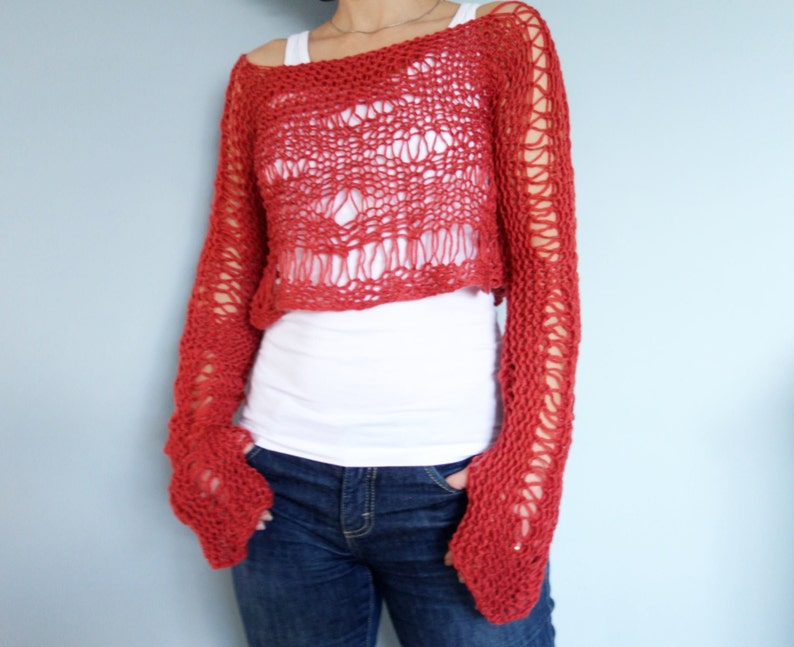 May include: A red crocheted sweater with a loose, open knit. The sweater has long sleeves and a cropped length. The sweater is made with a chunky yarn and has a relaxed fit.