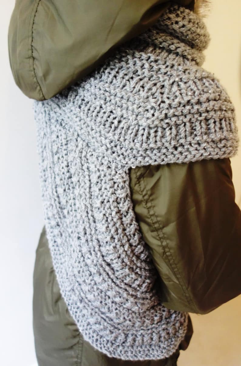 Puede incluir: Una bufanda de punto gris con un patr&oacute;n texturizado, puesta sobre una chaqueta verde con capucha.