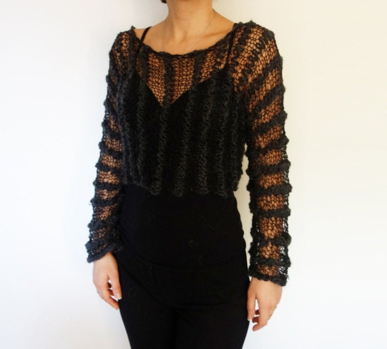 May include: A black, open-knit sweater with long sleeves. The sweater has a loose fit and a cropped length.