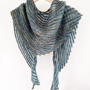 May include: A teal and gold striped knitted shawl with a fringed edge. The shawl is draped over a wooden hanger.