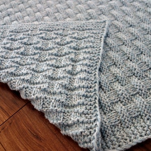 May include: A blue knitted blanket with a woven pattern on one side and a chevron pattern on the other side.