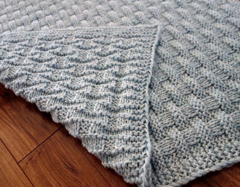 May include: A blue knitted blanket with a woven pattern on one side and a chevron pattern on the other side.