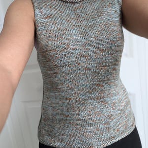 May include: A sleeveless knit top in a speckled pattern of blue, brown, and gray. The top has a scoop neckline and a fitted silhouette. The fabric appears to be a soft, lightweight yarn, suitable for warmer weather.