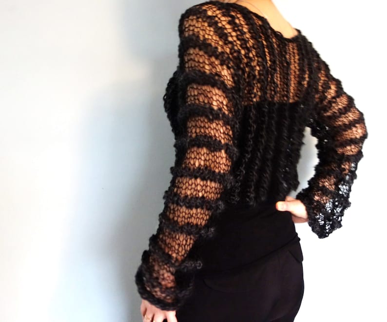 May include: A black, open-knit sweater with a loose fit and long sleeves. The sweater has a striped pattern and is made of a soft, lightweight yarn.