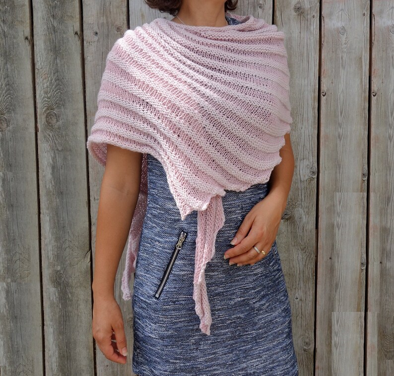 May include: A pink knitted shawl with a delicate, openwork design. The shawl is draped over a person's shoulders and is tied at the neck.