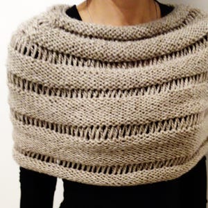 May include: A beige knitted shawl with a lacy pattern. The shawl has a wide, open neckline and is made of a soft, lightweight yarn.