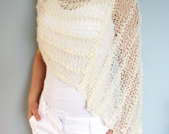 May include: A white crocheted shawl with a delicate openwork pattern. The shawl is draped over the shoulders of a person wearing a white shirt and white pants.
