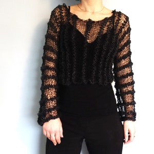 May include: Black knitted sweater with a loose fit and a lacy, open-weave design. The sweater has long sleeves and a round neckline.