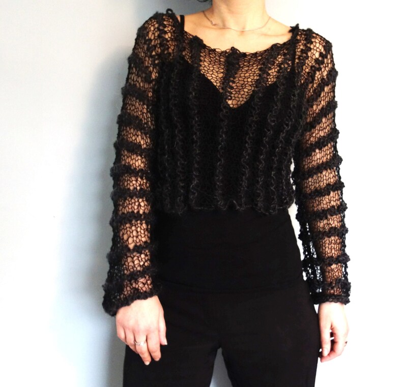 May include: Black knitted sweater with a loose fit and a lacy, open-weave design. The sweater has long sleeves and a round neckline.