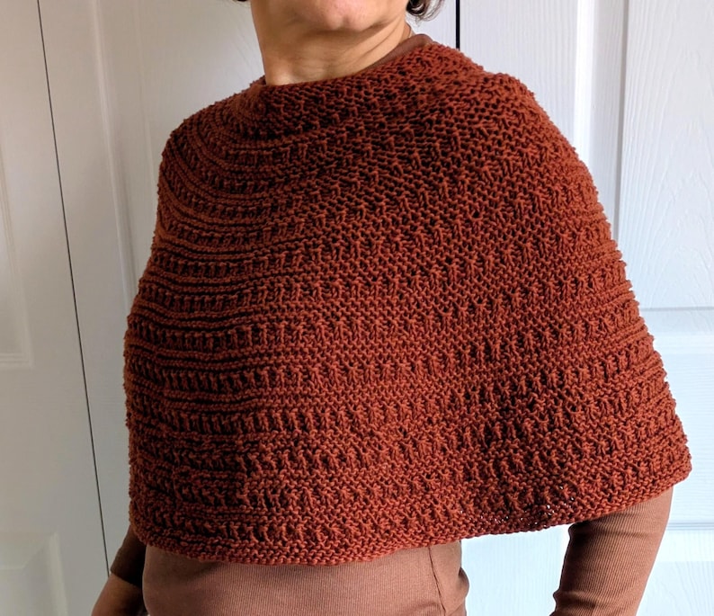 Pode incluir: Um poncho de malha na cor ferrugem com um padr&atilde;o texturizado de carreiras horizontais de pontos. A pe&ccedil;a possui um decote redondo, cobre a parte superior do tronco e apresenta uma constru&ccedil;&atilde;o de malha consistente.