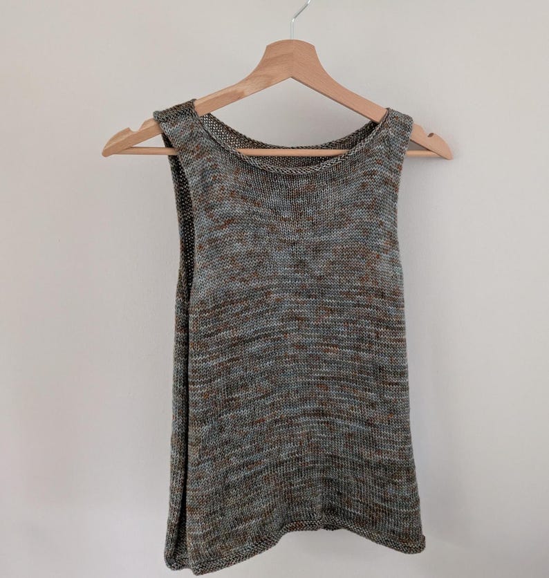 May include: A sleeveless knit top in a neutral color palette of gray, brown, and blue, hanging on a wooden hanger. The top has a scoop neckline and a slightly flared shape.