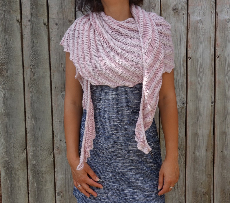 May include: A pink and white striped knitted shawl with a scalloped edge. The shawl is draped around a person's shoulders and neck.