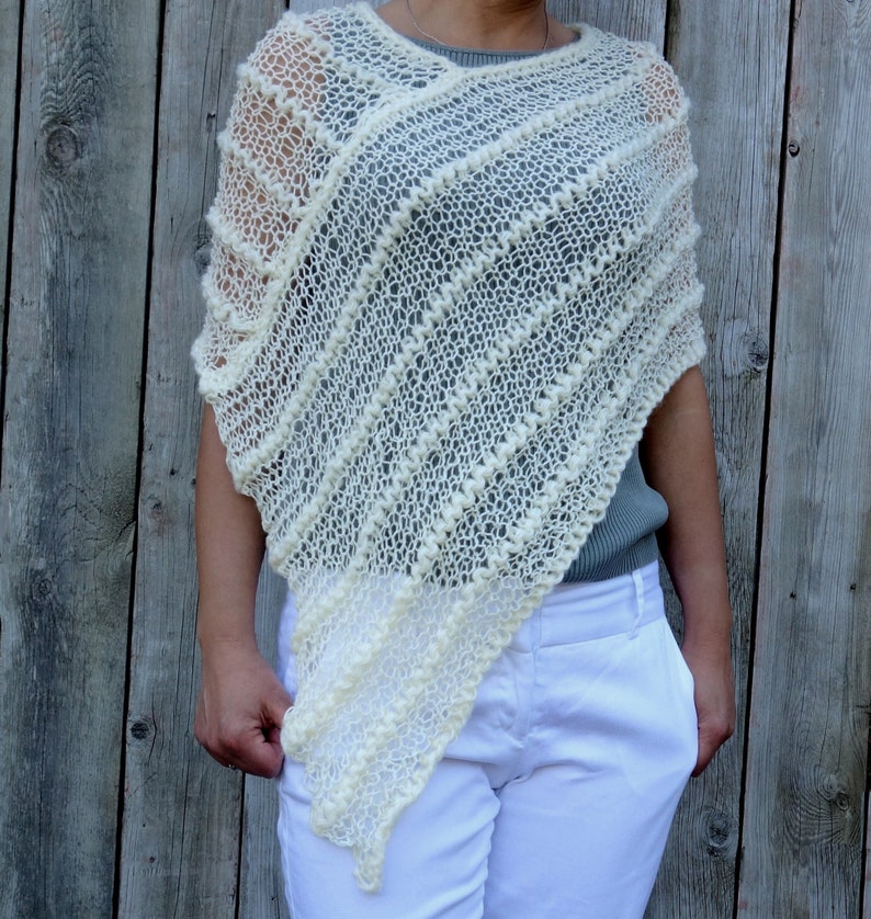 May include: A white crocheted poncho with a textured design. The poncho is made of a lightweight yarn and has a loose, flowing fit.