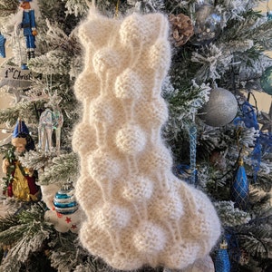 以下が含まれることがあります： ふわふわの質感とユニークな泡模様の白いニットの靴下。靴下はクリスマスツリーに飾られています。