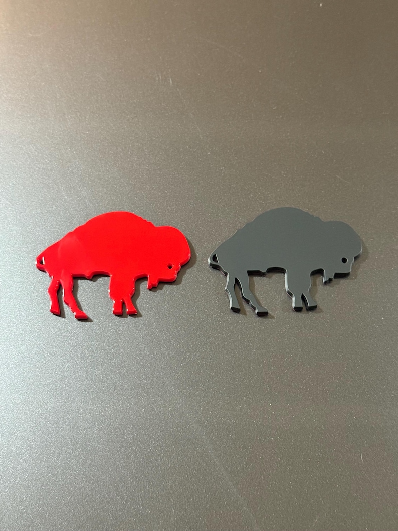 May include: Two bison-shaped cutouts. One is bright red, the other is dark gray. Both have a smooth, flat surface and are placed on a gray background. The bison are facing left, with their legs and heads clearly defined.