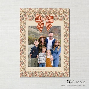 Könnte beinhalten: Weihnachtskarte mit einem Familienfoto in einem cremefarbenen Rahmen. Der Rahmen ist von einem Blumenmuster und einer großen orangefarbenen Schleife oben umgeben. Die Worte "merry christmas" und "the smiths" stehen unten.