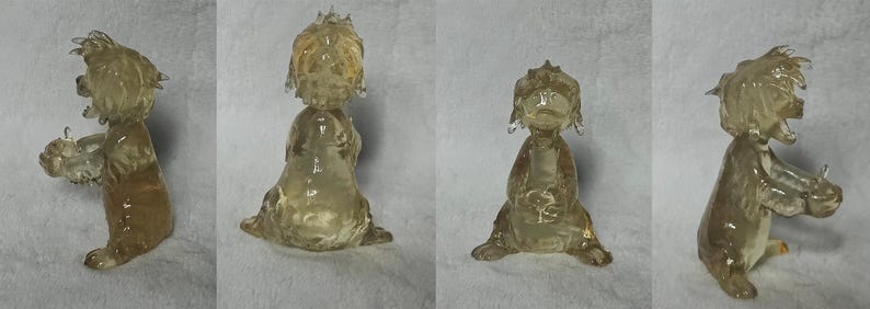 Puede incluir: Una figurita de vidrio transparente de un perro de dibujos animados con un tinte marr&oacute;n. El perro est&aacute; sentado sobre sus patas traseras con las patas delanteras levantadas. La figurita mide aproximadamente 15 cm de alto.