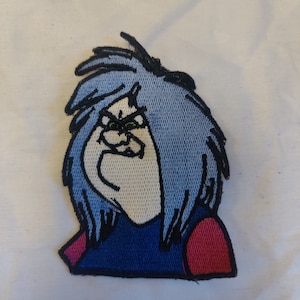 May include: Embroidered patch featuring a cartoon character with blue hair and an angry expression. The character has a light skin tone, a blue shirt, and red accents. The patch is outlined in black.