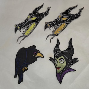 May include: Four embroidered patches featuring characters from a fantasy film. Includes two black dragon heads with yellow and white accents, a black raven with a yellow beak, and a green-skinned woman with black horns and a purple collar.