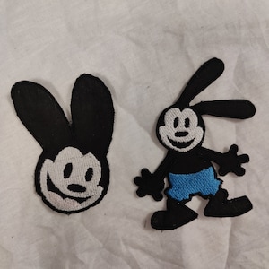 May include: Two black and white embroidered patches of a cartoon character with rabbit ears. One patch is a close-up of the character's face and the other is a full-body image of the character wearing blue shorts.